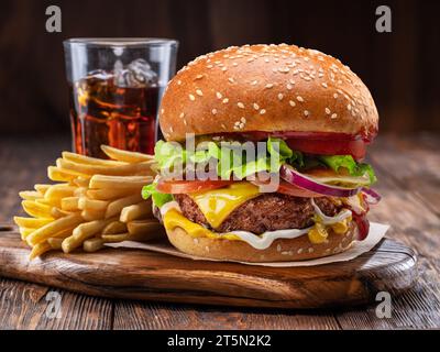 Gustosi cheeseburger o hamburger, bicchiere di cola e patatine fritte su vassoio di legno primo piano. Foto Stock