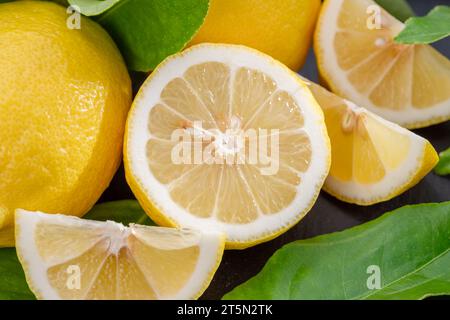Frutti di limone maturi con fette e foglie di limone su una tavola di pietra grigia. Un bel fondo di agrumi per i tuoi progetti. Foto Stock