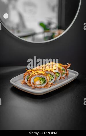 Sushi roll con fiocchi di tonno, gamberi tempura, mango e cetriolo su un piatto da vicino. Foto di alta qualità Foto Stock