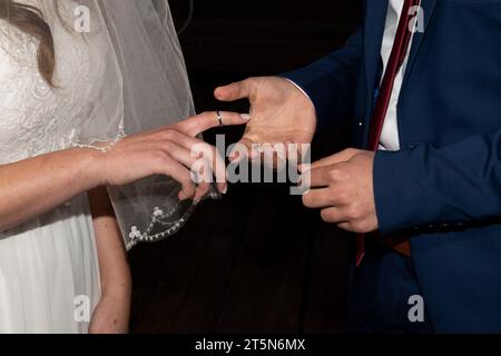 Una sposa estende la mano e il dito per ricevere l'anello acquistato dallo sposo durante una cerimonia di nozze ebraica. Foto Stock