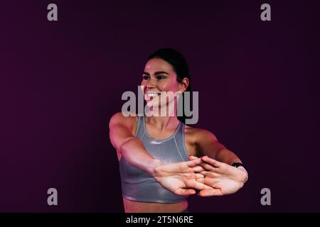 Primo piano di una giovane donna sorridente che si stende e piega le mani su uno sfondo magenta in studio Foto Stock