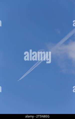 Una perfetta giornata estiva di sole con un aereo e sentieri di condensazione diretti verso una luna visibile in lontananza Foto Stock