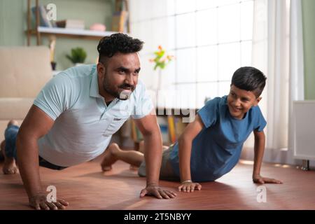 Padre indiano gioioso con il figlio che fa esercizi di push up a casa - concetto di fitness gioioso, stile di vita attivo e abitudini sane Foto Stock