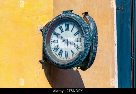 Il vecchio orologio rotondo è montato su un muro giallo intemprato . Orologio su una strada affascinante in una pittoresca città europea Foto Stock