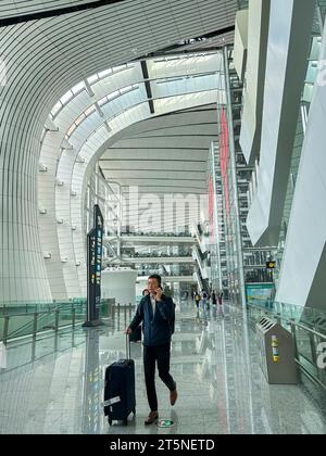 Pechino, Cina, uomo che viaggia con la valigia, parla sullo smartphone, vista interna dell'aeroporto internazionale di Pechino Daxing, terminal, hall (credito architetto: Zaha Hadid) Foto Stock