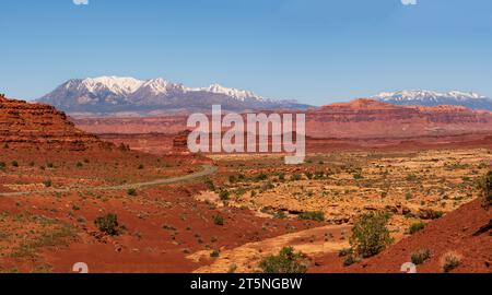 Vista panoramica di una strada desertica nel sud dello Utah, Stati Uniti, con montagne innevate all'orizzonte e cielo azzurro. Foto Stock