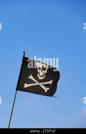 Jolly Roger, Skull e Crossbones bandiera pirata nera contro il cielo blu. Foto Stock