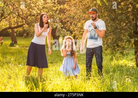 Figlia che soffia il tarassolo con i suoi genitori Foto Stock