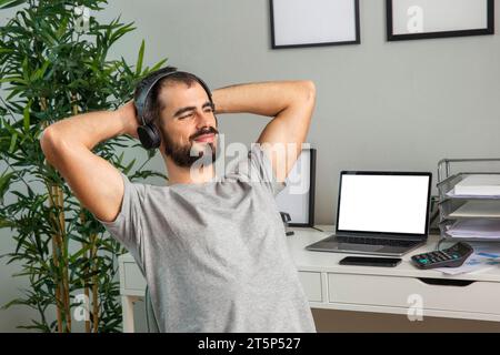 Uomo che usa le cuffie mentre lavora da casa Foto Stock