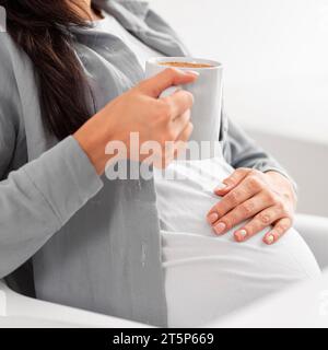 Vista laterale donna incinta che tiene a casa tazza caffè Foto Stock