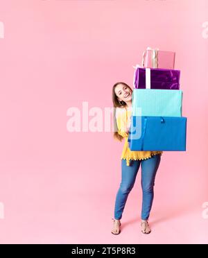 Donna felice che tiene una pila di colorate scatole regalo sullo sfondo rosa Foto Stock