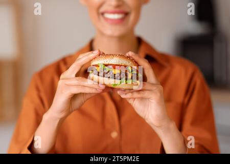 Primo piano del sorriso della donna mentre tiene un delizioso hamburger Foto Stock