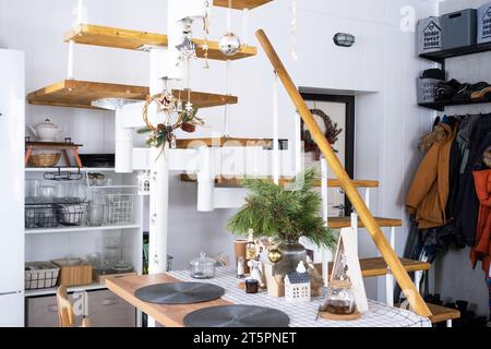 Decorazioni natalizie natalizie in cucina bianca, moderni interni soppalchi bianchi con scala modulare in metallo con gradini in legno. Anno nuovo, atmosfera, casa accogliente. Foto Stock