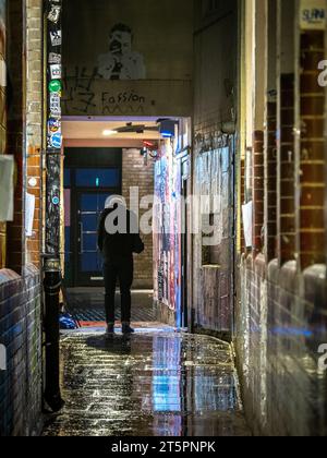 Un uomo solitario silhoutted in un vicolo buio e bagnato cosparso di graffiti a Soho, Londra Foto Stock