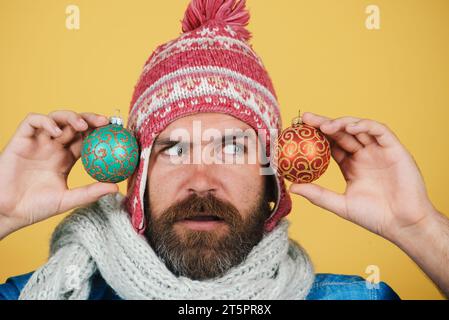 Uomo barbuto in abiti invernali con palline multicolori sull'albero di Natale. Un uomo sorpreso con le decorazioni natalizie. Vacanze invernali. Natale decorativo Foto Stock