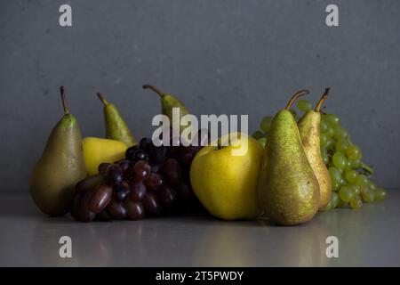 Natura morta dei frutti autunnali con pere, mele e uva su fondo grigio Foto Stock