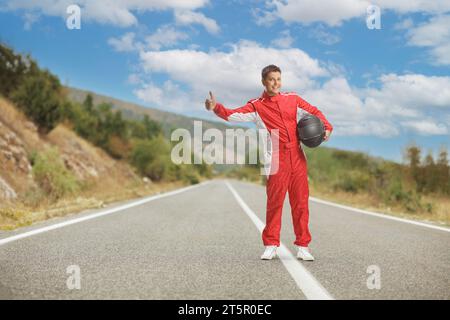 Scatto completo di un pilota in costume rosso con un casco e un autostop su una strada aperta Foto Stock