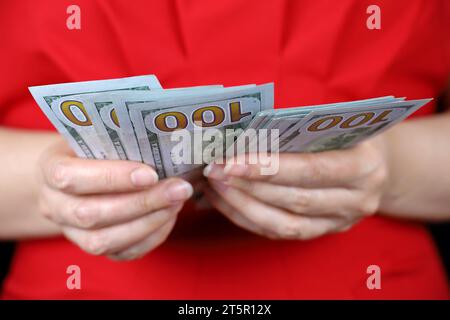 Dollari USA in mano femminile da vicino, la donna in vestito rosso conta i soldi. Concetto di tangente, stipendio, assistenza finanziaria o prestito Foto Stock