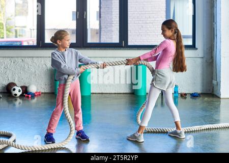 ragazze allegri in abbigliamento sportivo che tirano la corda per il fitness e sorridono allegramente l'una con l'altra, sport Foto Stock