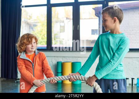 due ragazzi preadolescenti in abbigliamento sportivo che tirano la corda per il fitness e sorridono l'un l'altro, sport infantile Foto Stock