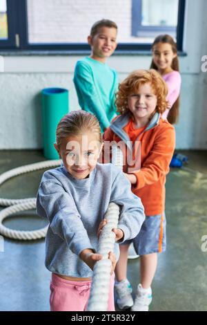 quattro allegri bambini preadolescenti che giocano a tiro e guardano la macchina fotografica in palestra, sport per bambini Foto Stock