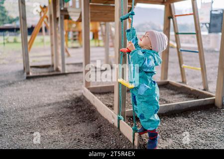 La bambina sta cercando di raggiungere il gradino superiore di una scala di corda in piedi sui piedi Foto Stock