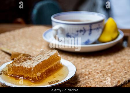 Disposizione mattutina su un tavolo di legno sul balcone, libri da leggere, tazza di tè naturale, teiera, miele biologico della fattoria, foglie di tè verde fresco e frutta biologica Foto Stock