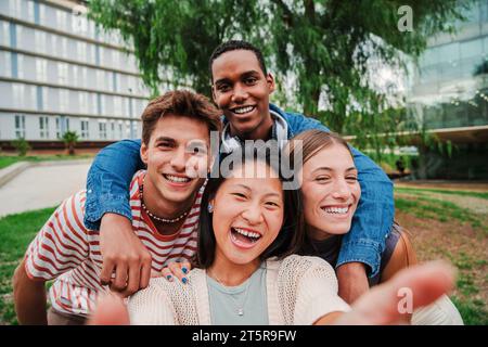 Gruppo di giovani studenti delle scuole superiori multirazziali che scattano un selfie ritratto all'esterno con un sorriso toothy che guarda la fotocamera ridere e divertirsi insieme. Ragazzi felici e amichevoli che scattano una foto. Foto di alta qualità Foto Stock