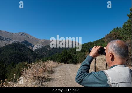 Un uomo che osserva attraverso il binocolo. Osservazione della fauna selvatica. Birdwatching. Foto Stock