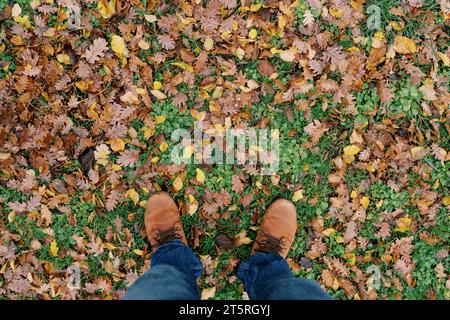 I piedi degli uomini con gli stivali poggiano su foglie cadute sull'erba verde. Vista dall'alto Foto Stock