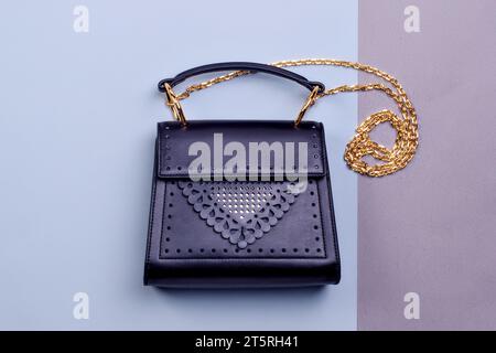 Elegante borsa da donna in pelle nera con design traforato originale, catena a spalla dorata e manico superiore su sfondo bicolore. M. Creativo Foto Stock