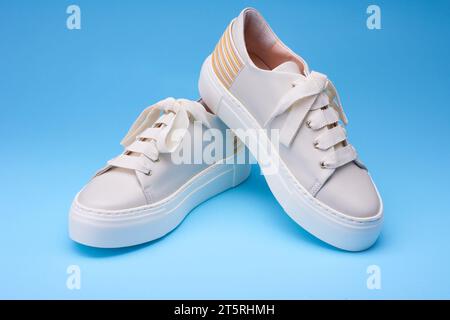 Vista ravvicinata delle sneaker moderne e alla moda su sfondo blu. Dettagli in pelle beige, pastello e giallo sul retro. Scarpe urban style conce Foto Stock
