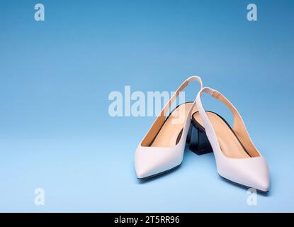 Un paio di eleganti scarpe bianche a punta con retro aperto e tacco nero svasato su sfondo blu sfumato. Scarpe eleganti da donna Foto Stock