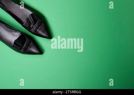 Eleganti scarpe da donna in pelle nera a punta con dettagli increspati e volant nell'angolo superiore sinistro di un morbido sfondo verde. Blog di moda Foto Stock