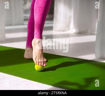 Massaggio per i piedi con palla da tennis. Donna che pratica l'auto-massaggio dei piedi con una palla da tennis. Fisioterapia, riflessologia. Allentamento della tensione nella planta Foto Stock