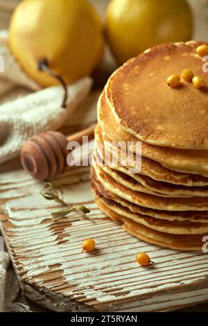Frittelle di banana impilate su un piatto di legno pallido, due pere sullo sfondo, frutti di bosco spinoso e un cucchiaio di miele. Un elemento di festa. Nutriti Foto Stock