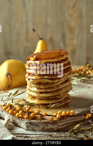 Un piatto di legno con i classici pancake americani versati con miele, due pere, un ciuffo di spina dorsale. Una componente di festa. Blog ricetta po Foto Stock