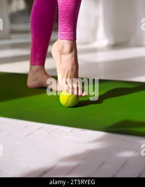 Massaggio con palla da tennis per i piedi. Donna che pratica l'auto-massaggio dei piedi con una palla da tennis. Fisioterapia, riflessologia. Riduzione della tensione nel plantare Foto Stock