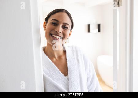 Ritratto di una donna birazziale felice che indossa un accappatoio bianco in bagno Foto Stock