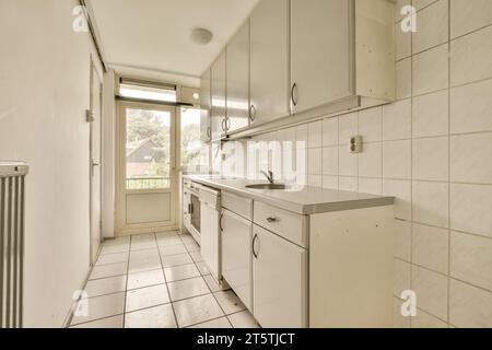 una cucina con piastrelle bianche sul pavimento e armadietti all'angolo, che guardano verso l'ingresso della porta sul retro Foto Stock