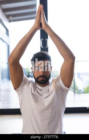 Rilassato uomo birazziale seduto, praticando yoga, chiudendo gli occhi e meditando in una stanza soleggiata a casa Foto Stock