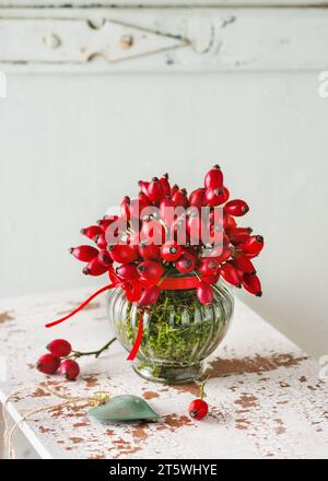 Splendido bouquet di fianchi di rose in vaso di vetro vintage come decorazione autunnale. Natura morta rustica floreale. Arredamento domestico. Copia spazio. Foto Stock