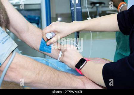 Inserimento di un catetere in una vena nel braccio di un paziente in ospedale prima dell'intervento chirurgico. Somministrazione della soluzione medicinale per via endovenosa. Le mani del medico inseriscono un ago nel braccio di un uomo. Foto Stock