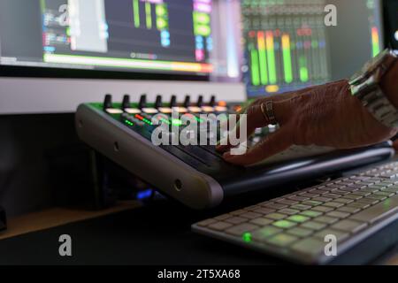 La mano di un tecnico del suono regola i cursori su una console di missaggio audio, mostrando il lato tecnico della produzione musicale e la precisione di missaggio. Foto Stock