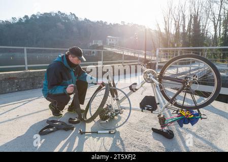 Un ciclista uomo ripara una bicicletta (mountain bike) con pneumatico sgonfio durante un'escursione. Concetto di imprevisto e sfortuna Foto Stock