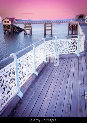 Il Mumbles Pier a Swansea, Galles, all'alba/al tramonto, con sfumature pastello, aspetto pulito con bellezza marina e rilevanza storica. Molo iconico per i turisti Foto Stock