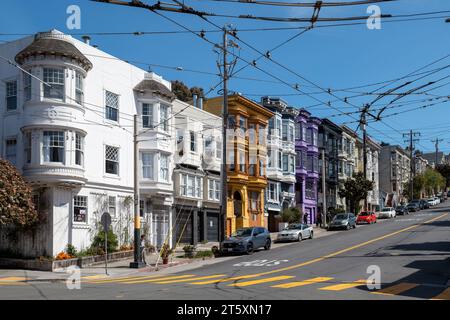 Castro Street, San Francisco, California, USA - 23 aprile 2023: Case colorate su una strada ripida con auto parcheggiate su strada asfaltata con segni gialli e. Foto Stock