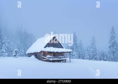 Una remota cabina di montagna in mezzo a un boschetto di abeti innevati su un altopiano boscoso in inverno. Concetto di vacanze natalizie e vacanze invernali Foto Stock