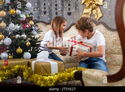 Bambina e ragazzo in casa con regalo in studio con interni natalizi Foto Stock