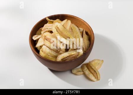 Patatine di banana in una ciotola di legno su un tavolo bianco Foto Stock